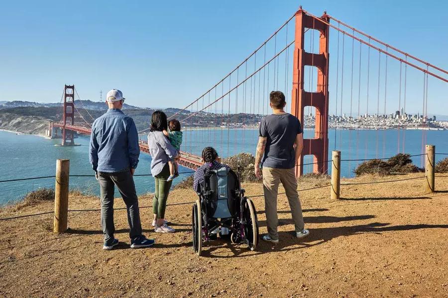 一群人, 包括一个坐轮椅的人, é visto por trás enquanto olham para a Ponte Golden Gate de Marin Headlands.